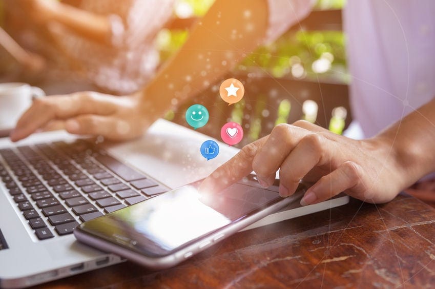 customer using laptop and phone with emojis floating above