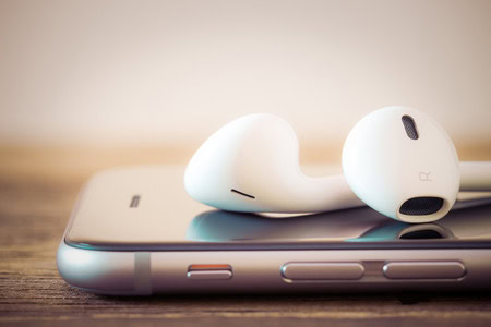 White earphones rest on top of a silver smartphone placed on a wooden surface.