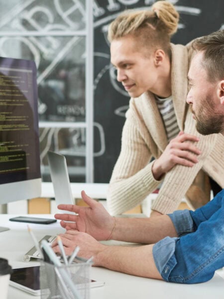 Positive program writers discussing computer language code while making web script on computer and discussing project in modern office