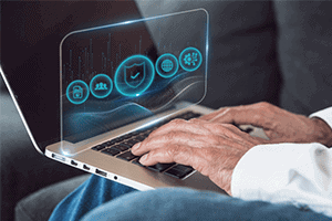 Person typing on a laptop with a virtual screen displaying security icons, including a lock, people, a shield, a gear, and a network symbol.