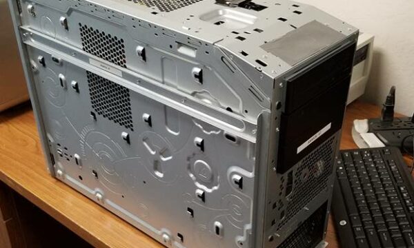 A silver computer tower case with side panel removed, showing vents and empty drive bays, is placed on a wooden desk next to a keyboard and mouse.
