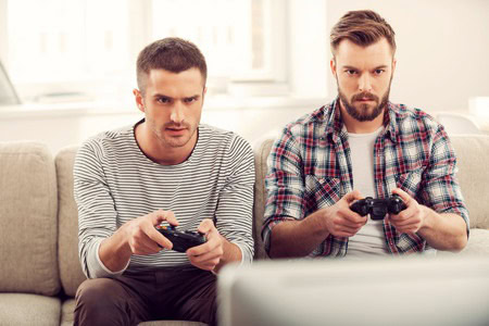 Two men sitting on a couch, intently playing video games with controllers in their hands.