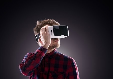Person wearing a virtual reality headset, dressed in a red and black plaid shirt, against a dark background.