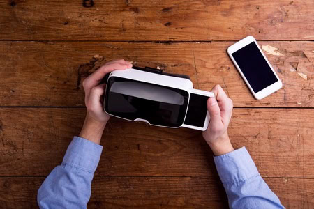 Person holding a VR headset on a wooden table, with a smartphone placed nearby.